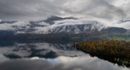 Low clouds covering majestic mountain reflecting on lake bohinj in autumnの写真素材