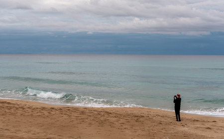 Photographer taking pictures of beautiful seascape with dramatic sky in winter. Sandy beach