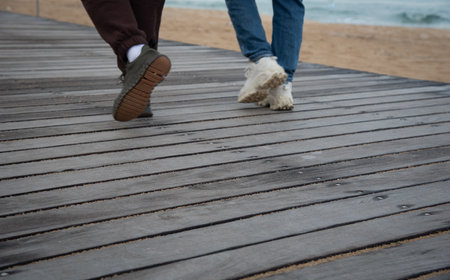 Two people walking on wooden boardwalk by the beachの写真素材