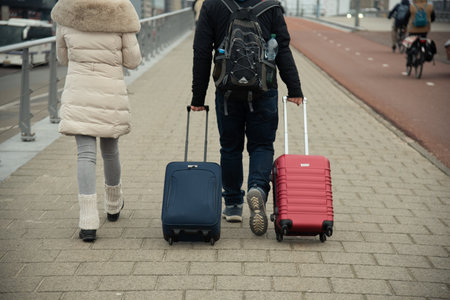 Two travelers stroll along a city sidewalk, pulling piece of travel luggage.の写真素材