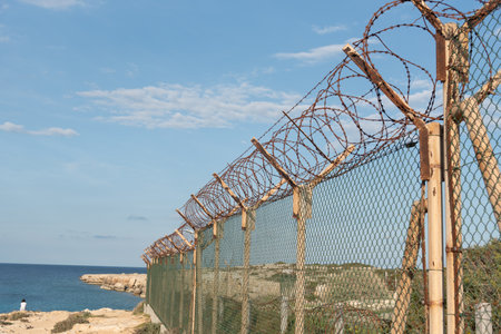 Security fence with barbed wire against a blue cloudy sky. Security border forbidden access. Military zoneの写真素材