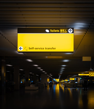 Illuminated signs guiding passengers to toilets and self-service transfer within a modern airport terminalの写真素材