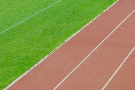 Red running track lines meeting green grass field in stadium, creating a dynamic and energetic sports backgroundの写真素材