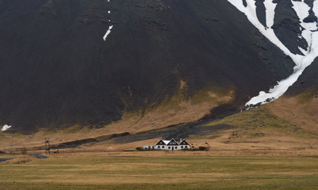 Icelandic landscape with farmhouses under volcanic mountain covered in snow in Iceland. . Southeast...