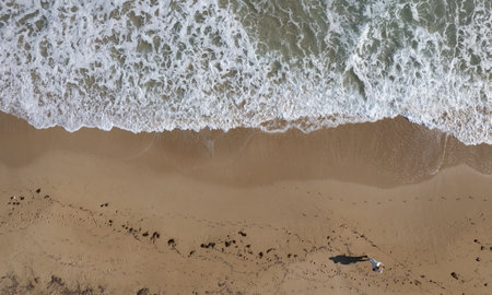 Aerial drone point of view of person walking on sand in a beach. Stormy waves idyllic beach in...