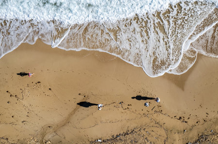 Aerial drone point of view of person walking on sand in a beach. Stormy waves idyllic beach in winter. Top view image of people in the sandy shoreの写真素材