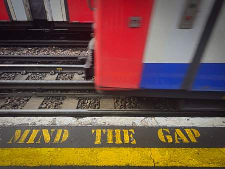 Yellow mind the gap text on a london subway platform with approaching train. Metro station warning signの写真素材