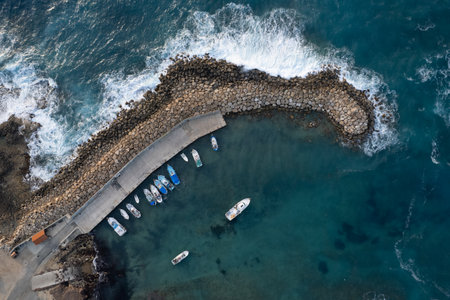 Drone aerial scenery of fishing boats moored at the harbor at the breakwater. Stormy waves at sea...