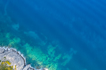 Drone aerial view of turquoise sea water meeting a rocky coastline on a sunny summer dayの写真素材
