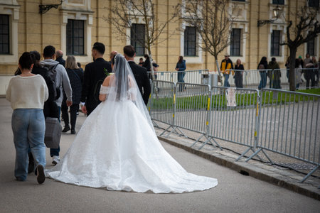 Austria, Vienna, October 25, 2025: Bride and groom walking together outdoors with a long white wedding dress train flowing behindのeditorial素材