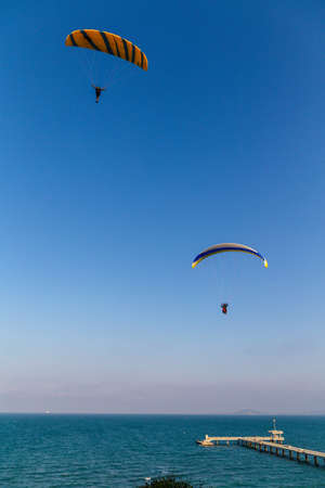 Paraglider flying over the sea coast in blue sky backgroundの写真素材