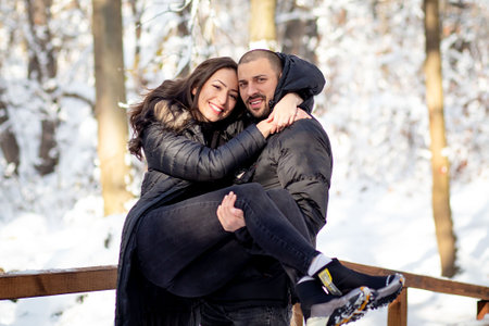 Man and woman in love hugging and kissing on a bridge. Snowy winter background.の写真素材
