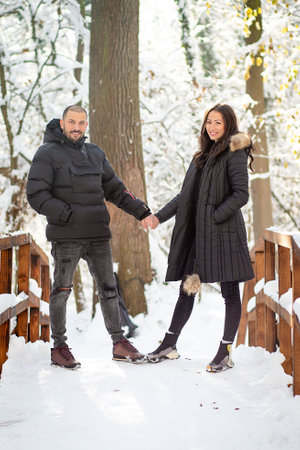 Man and woman in love holding hands on a bridge. Snowy winter background.の写真素材