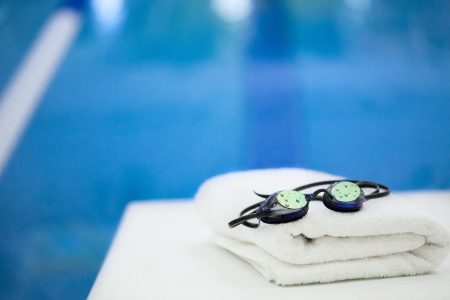 Reflective goggles with beads of water on them, sitting besides a swimming pool on a clean, white, nicely folded towel の写真素材