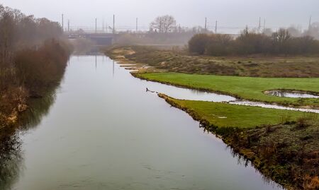 Water of a canal with reflections in the water and a foggy landscape surrounding itの写真素材