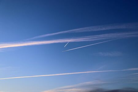 Aircraft condensation contrails in the blue sky inbetween some cloudsの写真素材