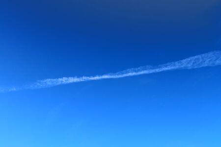 Aircraft condensation contrails in the blue sky inbetween some clouds