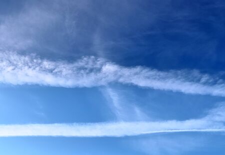 Aircraft condensation contrails in the blue sky inbetween some clouds