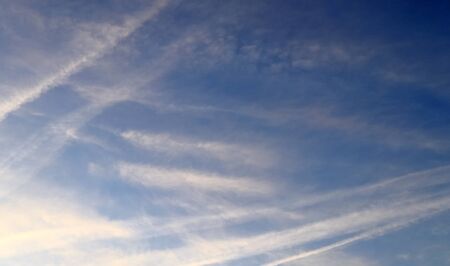 Aircraft condensation contrails in the blue sky inbetween some clouds