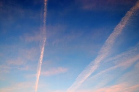 Aircraft condensation contrails in the blue sky inbetween some clouds