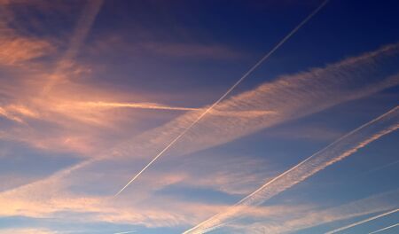 Aircraft condensation contrails in the blue sky inbetween some clouds