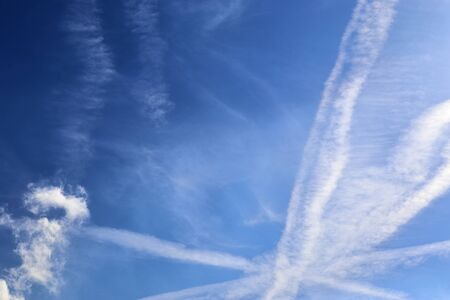 Aircraft condensation contrails in the blue sky inbetween some clouds