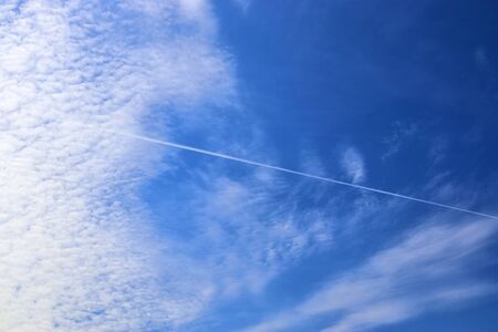Aircraft condensation contrails in the blue sky inbetween some clouds