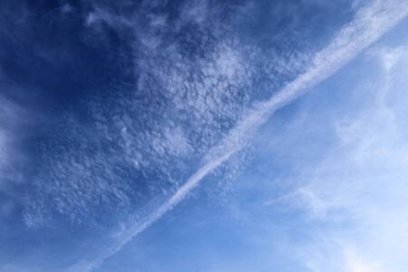 Aircraft condensation contrails in the blue sky inbetween some clouds