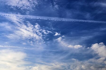 Aircraft condensation contrails in the blue sky inbetween some clouds