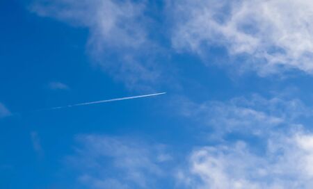 Aircraft condensation contrails in the blue sky inbetween some clouds