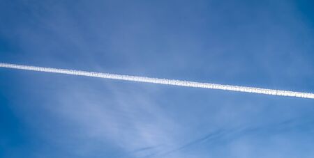 Aircraft condensation contrails in the blue sky inbetween some cloudsの写真素材