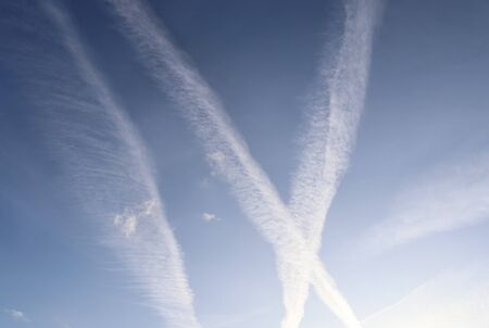 Aircraft condensation contrails in the blue sky inbetween some clouds