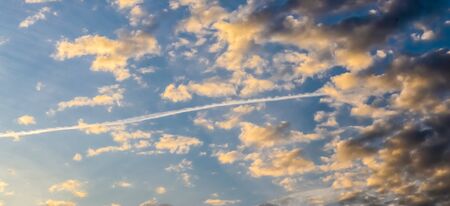 Aircraft condensation contrails in the blue sky inbetween some clouds
