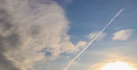 Aircraft condensation contrails in the blue sky inbetween some clouds