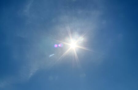 Beautiful view at bright sunbeams with some lens flares and clouds in a blue skyの写真素材