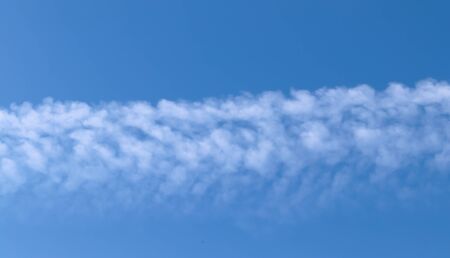 Aircraft condensation contrails in the blue sky inbetween some beautiful cloudsの写真素材