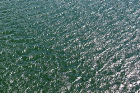 Detailed close up view on water surfaces with waves and ripples and the sunlight reflecting at the surfaceの写真素材