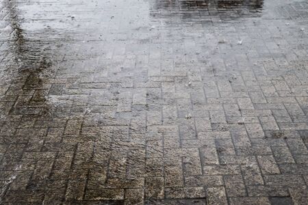 Heavy rain drops falling on city street during downpour. Wet ashpalt road texture.の写真素材
