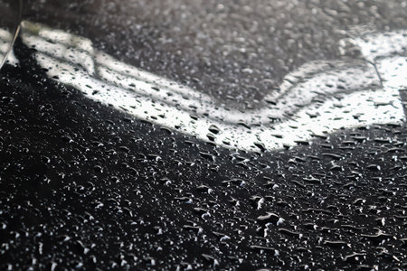 Rain drops on a black metallic car surface in a closeup viewの写真素材