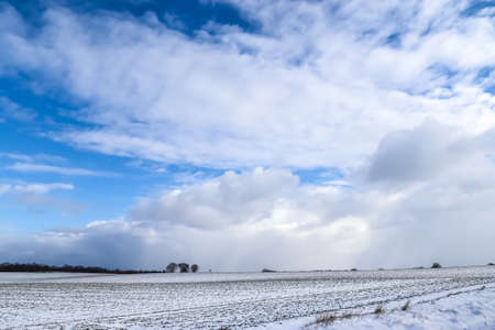Beautiful clouds in the sky looking over a snow covered agricultural fieldの写真素材