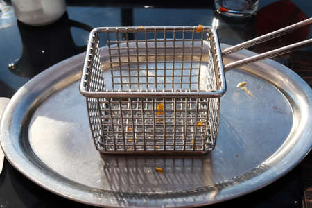 Empty metallic deep fryer on a table with some little fries piecesの写真素材