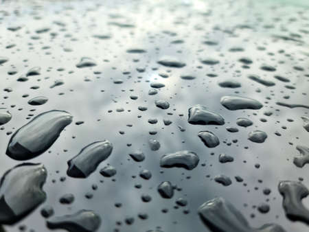 Rain drops on a black metallic car surface in a closeup view