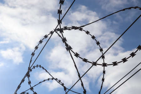 Barbed wire against a cloudy sky on a big fence at a borderの写真素材