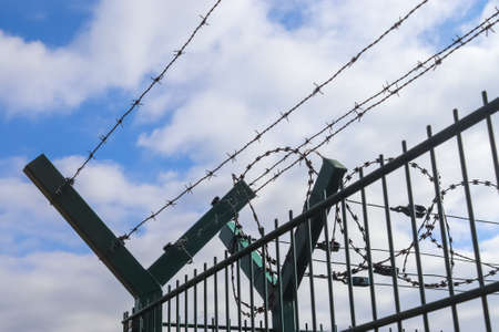 Barbed wire against a cloudy sky on a big fence at a borderの写真素材