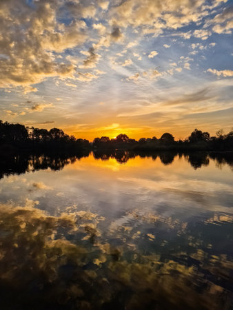 Beautiful golden sunset reflecting on calm lake water with cloudy sky