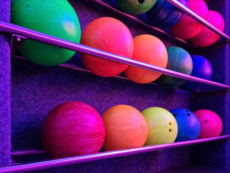 Colorful bowling balls resting on metal rack in illuminated shelves, ready for a fun gameの写真素材