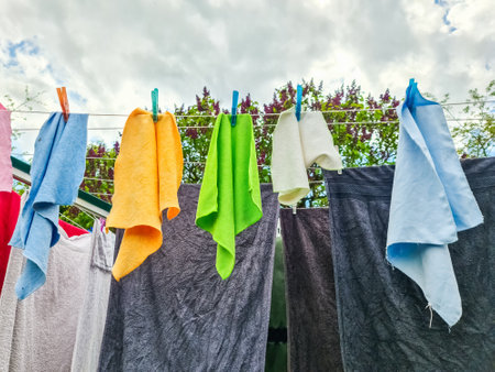 Colorful towels and rags drying on clothesline under cloudy sky