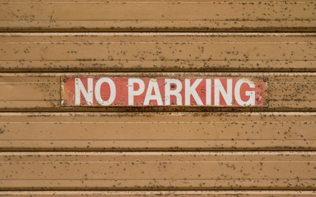 Weathered no parking sign indicating parking restrictions on a rusty metal rolling shutter doorの写真素材