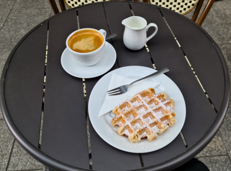 Freshly baked waffle served with coffee and milk on a table at an outdoor cafe, perfect breakfast or snackの写真素材