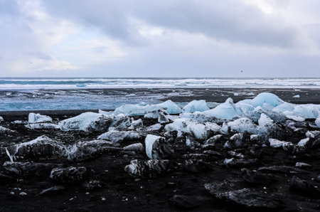 Icebergs from breidamerkurjokull glacier melting on diamond beach in iceland, creating a stunning contrast with the black sand and the cloudy skyの写真素材